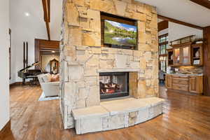 Unfurnished living room with beam ceiling, wood finished floors, high vaulted ceiling, and a stone fireplace
