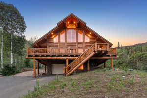 View of front of home with log siding, an attached garage, driveway, a deck, and a wooded view