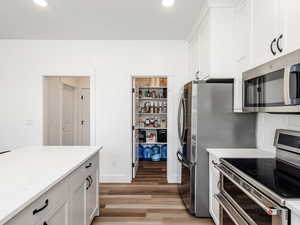 Kitchen with stainless steel appliances, light wood finished floors, white cabinets, recessed lighting, and light stone counters