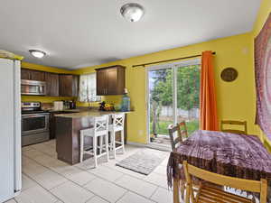 Kitchen with appliances with stainless steel finishes, dark brown cabinets, a breakfast bar, a peninsula, and stone counters