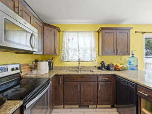 Kitchen featuring appliances with stainless steel finishes, light stone countertops, and light tile patterned floors