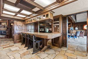 Bar with ornamental molding, stone flooring, coffered ceiling, wooden walls, and beamed ceiling