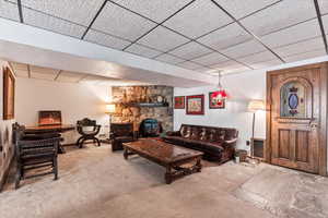 Living area with a drop ceiling, carpet flooring, and a wood stove