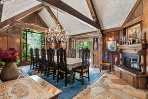 Dining space with a chandelier, beam ceiling, high vaulted ceiling, a glass covered fireplace, and a textured ceiling
