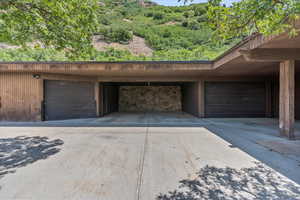 Garage with concrete driveway, a wooded view, and a carport