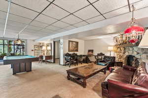 Living room with carpet floors, pool table, a paneled ceiling, and a fireplace