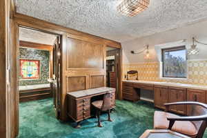 Office area with wallpapered walls, carpet floors, a textured ceiling, and built in desk