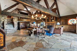 Living room with high vaulted ceiling, stone floors, beamed ceiling, a fireplace, and a chandelier