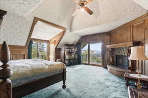 Bedroom with lofted ceiling, access to outside, carpet, multiple windows, and a fireplace with raised hearth