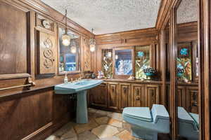 Bathroom featuring wood walls, stone finish flooring, a textured ceiling, and ornamental molding