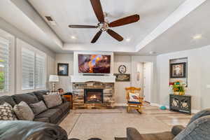 Living area with ceiling fan, wood finished floors, a stone fireplace, a raised ceiling, and recessed lighting