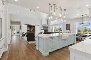 Kitchen featuring light countertops, a barn door, open floor plan, a large island with sink, and wood finished floors