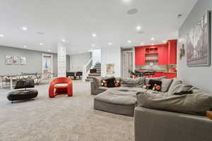 Carpeted living room featuring bar with sink, stairway, recessed lighting, and ornate columns