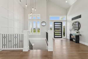 Foyer with wood finished floors, a decorative wall, high vaulted ceiling, and healthy amount of natural light