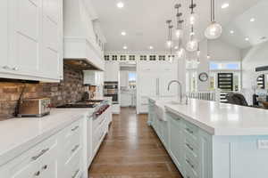 Kitchen featuring appliances with stainless steel finishes, white cabinetry, light countertops, backsplash, and a large island with sink