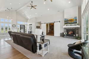 Living room featuring high vaulted ceiling, a ceiling fan, a barn door, beam ceiling, and wood finished floors