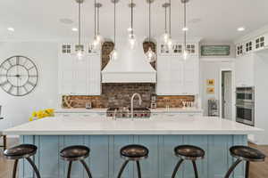 Kitchen featuring double oven, premium range hood, backsplash, white cabinetry, and recessed lighting
