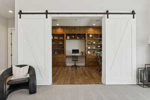 Office space featuring a barn door, recessed lighting, wood finished floors, and built in desk