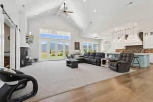 Living room with a barn door, high vaulted ceiling, ceiling fan, light wood-style flooring, and beamed ceiling