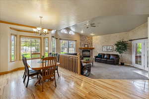 Dining room featuring vaulted ceiling, a textured ceiling, light wood-style flooring, a stone fireplace, and a ceiling fan