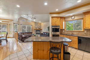 Kitchen featuring black dishwasher, black and stainless steel double oven, a center island, a breakfast bar area, and light tile patterned floors
