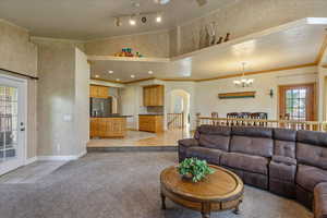 Living room featuring light tile patterned flooring, light colored carpet, a towering ceiling, crown molding, and a chandelier