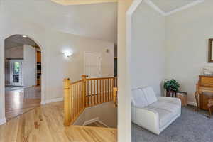 Corridor featuring arched walkways, light wood-style floors, and an upstairs landing