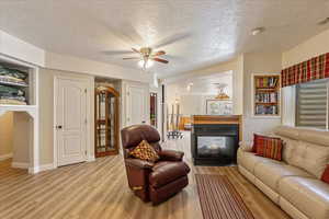 Basement family room with light wood-type flooring, a multi sided fireplace, ceiling fan, and built in shelves