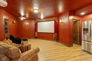 Cinema with wood finished floors, a ceiling fan, and framed wall screen.