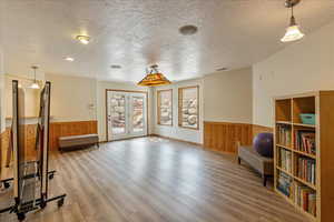 Unfurnished room with a wainscoted wall, wooden walls, a textured ceiling, wood finished floors, and french doors
