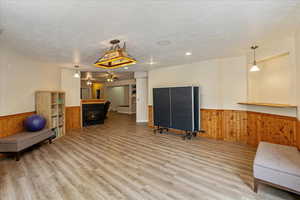 Exercise area featuring a wainscoted wall, a warm lit fireplace, a textured ceiling, wooden walls, and light wood-type flooring