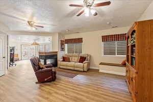 Basement family room featuring a ceiling fan, a textured ceiling, light wood-style floors, and a multi sided fireplace