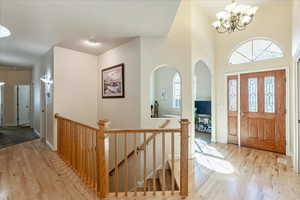 Entrance foyer with light wood finished floors, a chandelier, arched walkways, and a high ceiling