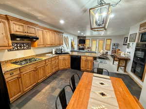 Kitchen with black appliances, under cabinet range hood, a textured ceiling, open floor plan, and stone tile flooring
