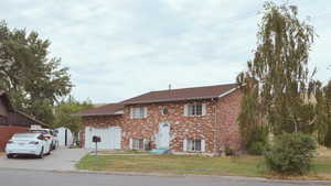 Split foyer home with concrete driveway, brick siding, a front lawn, an attached garage, and roof with shingles