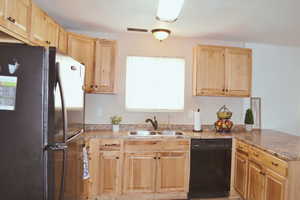 Kitchen with freestanding refrigerator, dishwasher, light brown cabinetry, a peninsula, and light stone counters