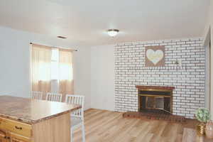 Kitchen featuring wood finished floors, a brick fireplace, and light brown cabinetry