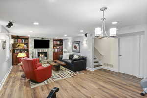 Living area with hardwood / wood-style floors, a stone fireplace, a chandelier, recessed lighting, and built in shelves