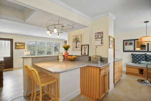Kitchen with a breakfast bar, crown molding, stone counters, brown cabinets, and hanging light fixtures