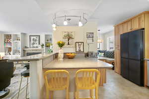 Kitchen featuring freestanding refrigerator, open floor plan, a kitchen bar, built in features, and a stone fireplace