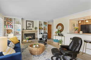Living room featuring wood finished floors, crown molding, a fireplace, and built in features