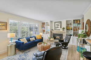 Living room featuring wood finished floors, ornamental molding, a textured ceiling, a fireplace, and built in features