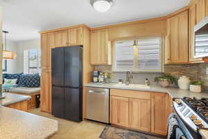 Kitchen with stainless steel appliances, decorative backsplash, light brown cabinetry, light countertops, and crown molding