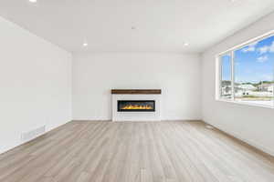 Unfurnished living room with light wood-style floors, recessed lighting, and a glass covered fireplace