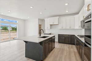 Kitchen featuring light wood-style flooring, white cabinets, stainless steel appliances, a center island with sink, and recessed lighting