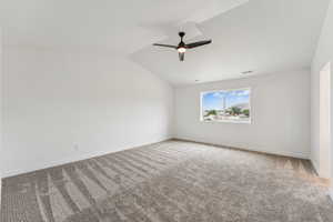 Spare room featuring carpet flooring, a ceiling fan, and vaulted ceiling