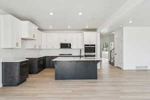Kitchen with white cabinets, recessed lighting, dark cabinets, an island with sink, and light wood-style flooring
