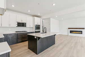 Kitchen featuring white cabinets, light countertops, light wood-type flooring, recessed lighting, and a kitchen island with sink