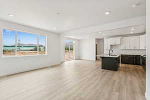 Kitchen featuring open floor plan, light wood finished floors, light countertops, a kitchen island with sink, and white cabinets