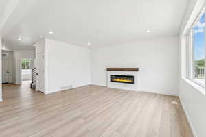 Unfurnished living room with light wood finished floors, recessed lighting, and a glass covered fireplace